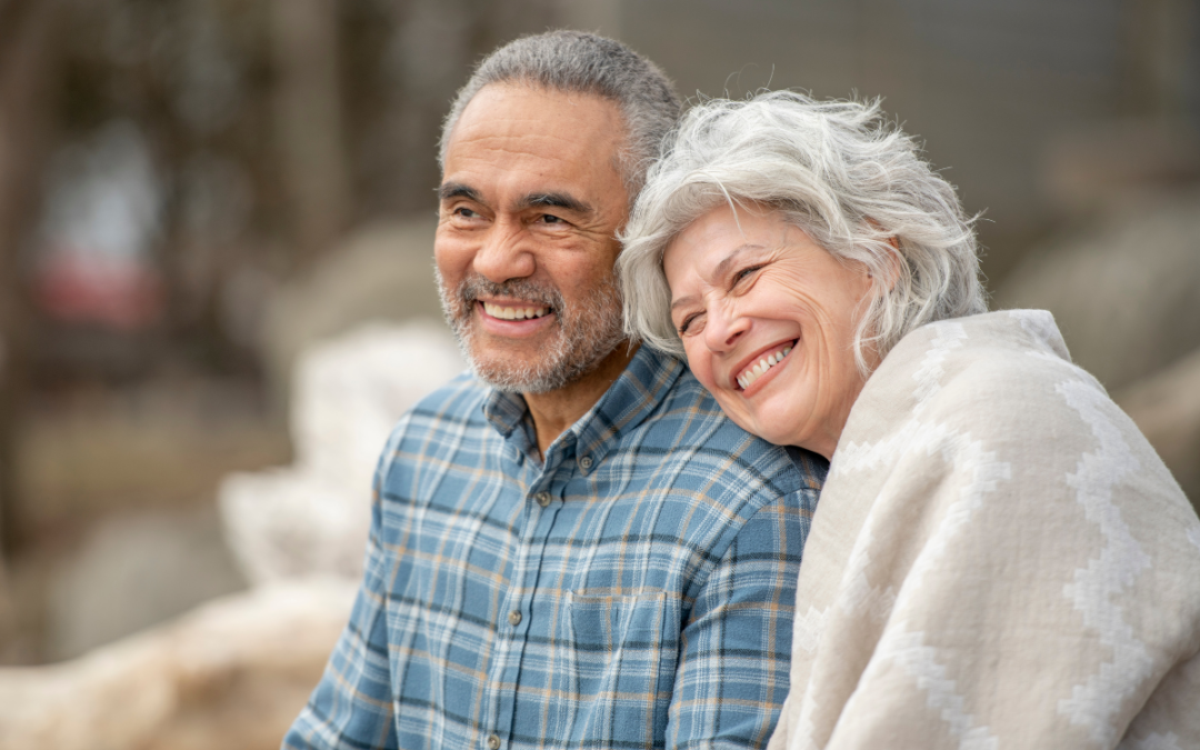 Elderly couple outside smiling, woman leaning on mans shoulder